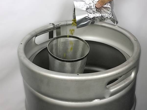 A hand is pouring hops into brewing filter on the kettle